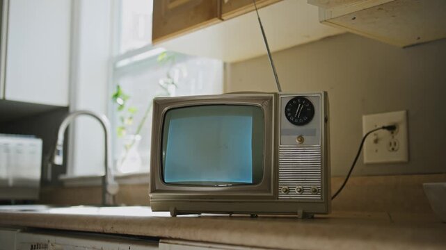 An old-fashioned black and white TV sits on a kitchen counter, displaying static. This retro setup evokes warm feelings of past entertainment and echoes the charm of bygone days