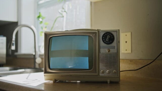 A charming retro television set stands in a vintage kitchen, showing black and white static. The warm light creates a cozy atmosphere, evoking feelings of nostalgia and the past