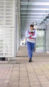 Vertical video: Leaving C 4 entrance, woman walking along path, checking phone and holding folders