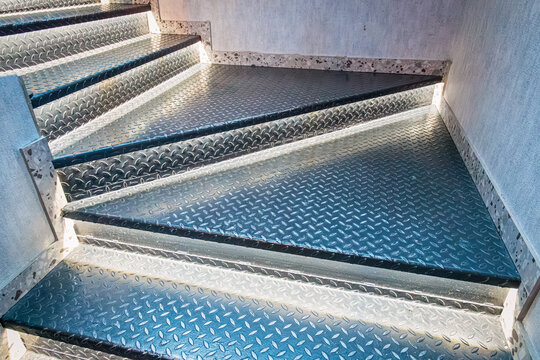 Industrial metal staircase with diamond plate texture on the steps and a black handrail, creating a strong architectural detail