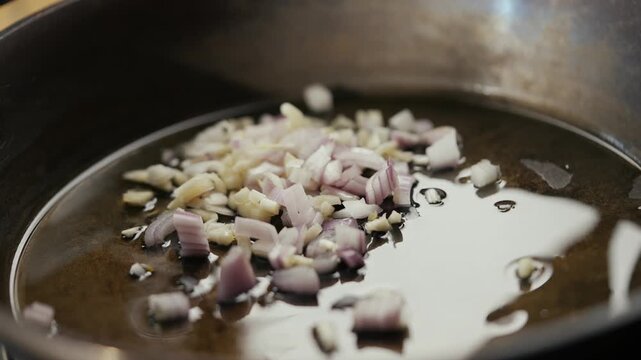 Oil heats in pan. Onion and garlic sizzle, sauteed. Wooden spoon stirs, releases aroma. Perfect for cooking tutorials, recipe videos, or food blogs