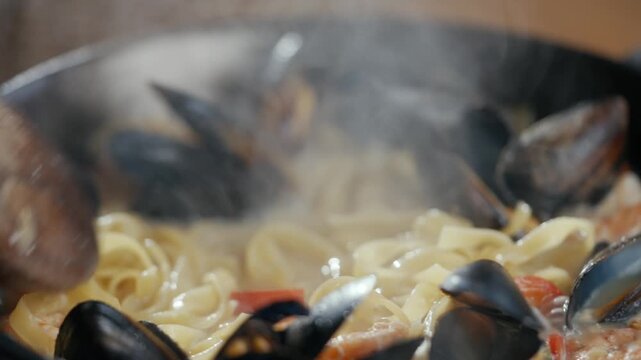 Steam rises from simmering pasta with mussels and shrimp. Hand stirs the dish with wooden spoon. Food looks fresh, aromatic, and deliciously warm. Perfect for recipes, restaurant ads