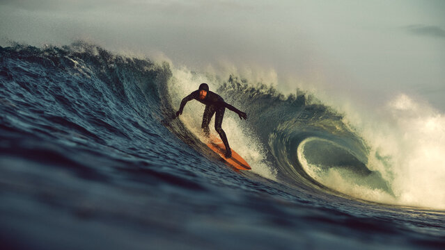 surfer taking off on big tubular wave at sunrise