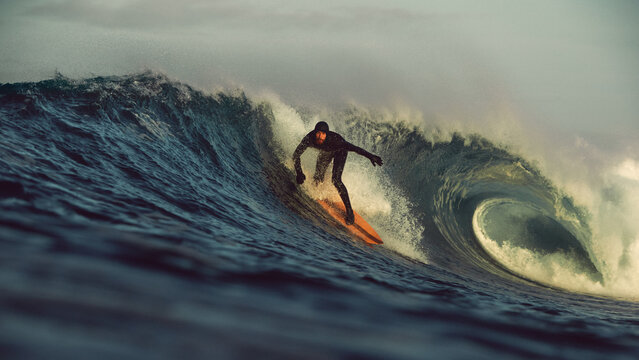 surfer taking off on big tubular wave at sunrise