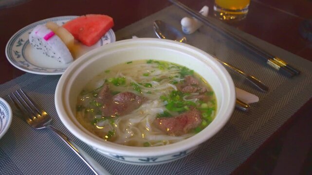 Steaming Hot Traditional Vietnamese Pho Beef Noodle Soup with Fresh Herbs and Sprouts Served in an Authentic Local Restaurant Setting in Vietnam