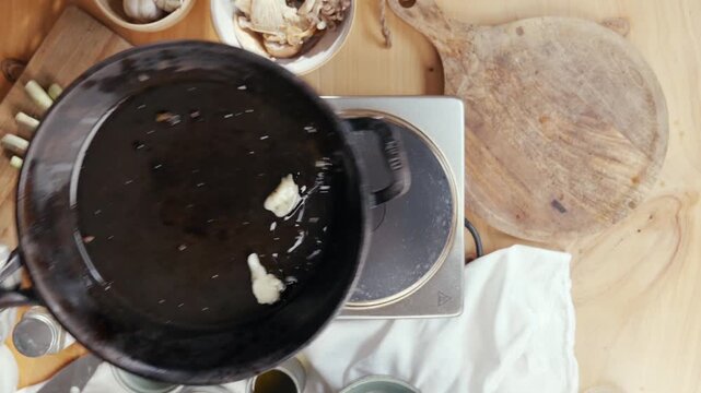 Top-down view of a black pot on a wooden table. Butter melts in the pan. Ingredients and kitchen tools surround the pot. Clean and organized cooking space. Ideal for cooking tutorials or recipe videos
