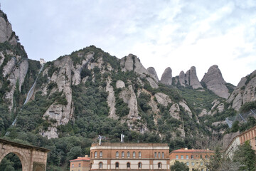 Fototapeta premium The unique jagged peaks of Montserrat mountain range rise majestically above lush green vegetation and buildings below