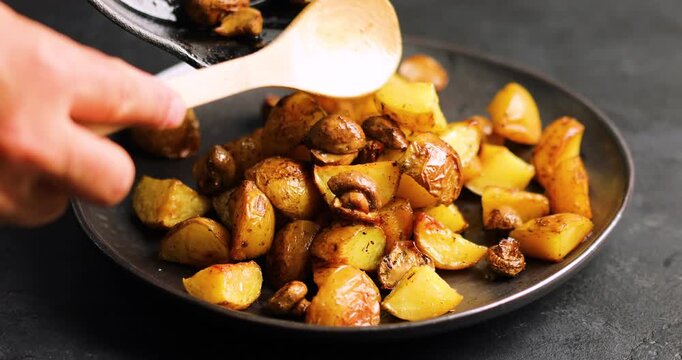 Baked potatoes with mushrooms in a plate on the table. Woman puts lunch from frying pan on plate	