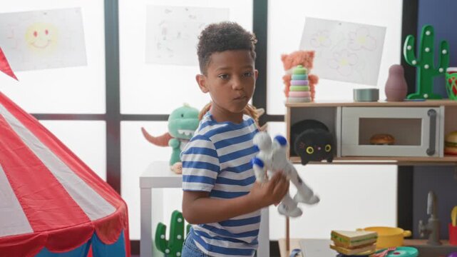 Boy holds white toy robot in right hand, arm raised while inspecting it among playroom toys in a studio; curiosity imagination.