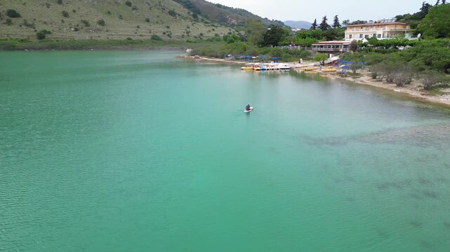 High angle aerial view of a father and his little daughter paddling together on a stand up paddleboard on the turquoise waters of Lake Kournas in Crete island, Greece. High quality 4k footage