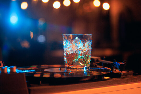 Whiskey glass on vinyl record with neon bar lights and retro music mood. Concept of whiskey menu, speakeasy lounge, analog music, alcohol brand advertising, and nightlife poster.