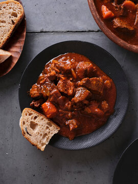 Slow cooked shredded beef served with bread on a black plate alongside a bowl of stew on a wooden table
