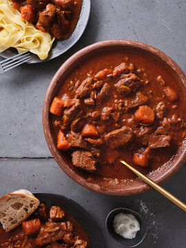Slow cooked shredded beef served with carrots and noodles on a table with bread and salt bowl nearby