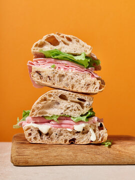 Fresh ciabatta sandwich with ham and lettuce on a wooden board against a bright orange background