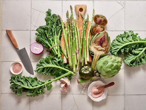 Fresh vegetables prepare for a healthy meal with kale, broccolini, artichoke, asparagus, and kumato tomatoes on a kitchen counter
