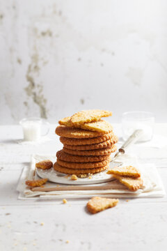 Stack of golden butter cookies on a white plate with crumbs on a rustic table.