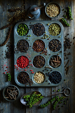 Flat lay of assorted peppercorn varieties in a vintage metal tray on rustic wood.