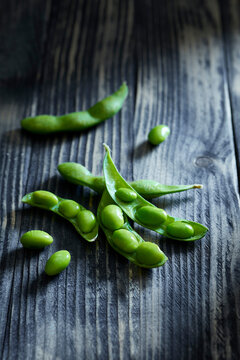 Fresh edamame pods with bright green soybeans on a dark rustic wooden table.