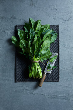 Fresh spinach bundle with rustic knife on a dark mat and stone background