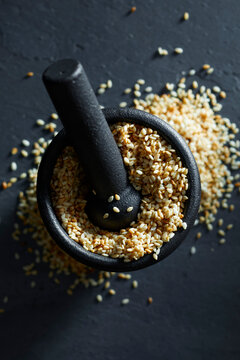 Golden sesame seeds in a black mortar with pestle on a dark background.