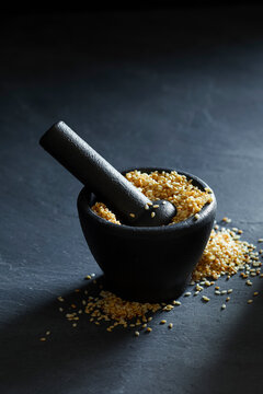 Golden sesame seeds in a black mortar with pestle on a dark background.