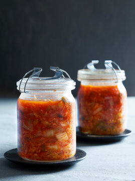 Glass jars filled with homemade kimchi on dark plates, moody background.