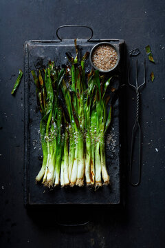 Charred, grilled spring onions sprinkled with coarse sea salt on a rustic tray.
