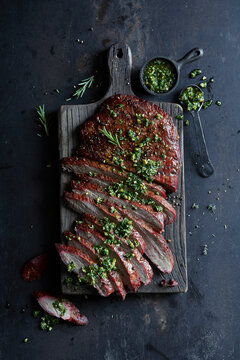 Sliced grilled flank steak topped with fresh chimichurri on a rustic wooden board.