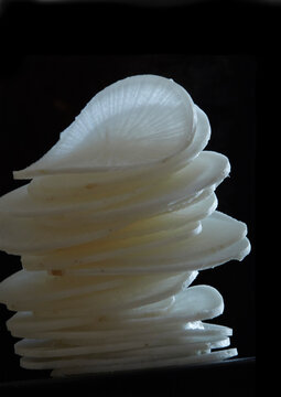 Stacked thin slices of fresh daikon radish in dramatic low-key lighting.