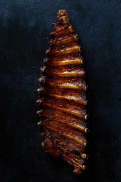 Glazed grilled pork spare ribs on a dark tray with coarse sea salt.