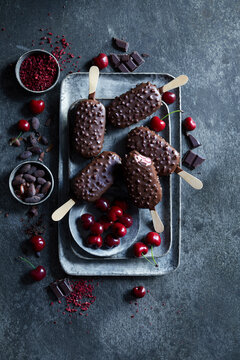 Chocolate coated cherry ice cream bars with crunchy cocoa nibs, styled with fresh cherries and chocolate on a dark moody background