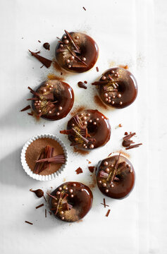 Chocolate glazed donuts topped with cocoa powder, chocolate shavings and sugar pearls, photographed from above