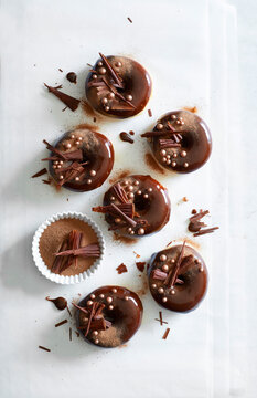 Chocolate glazed donuts topped with cocoa powder, chocolate shavings and sugar pearls, photographed from above