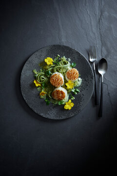 Gourmet food photography of seared scallops with herbs and edible flowers, plated on a stylish black stone plate for modern fine dining presentation