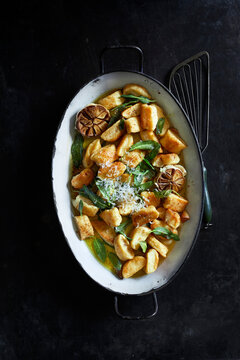 Golden pan-fried gnocchi tossed in sage butter with roasted garlic and grated cheese, served in a rustic enamel pan on a dark background