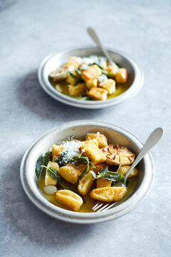 Top view of pan-fried gnocchi served with sage butter, roasted garlic and freshly grated Parmesan in rustic bowls