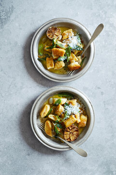 Top view of pan-fried gnocchi served with sage butter, roasted garlic and freshly grated Parmesan in rustic bowls