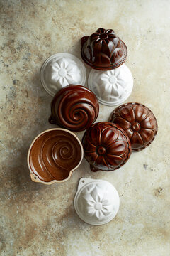 Assorted vintage ceramic pudding molds in brown and white arranged on a textured stone surface, photographed from above in soft natural light to highlight traditional shapes and glazed finishes