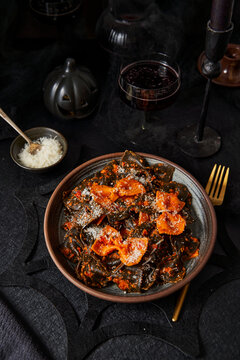 Black and orange pasta with parmesan on black table halloween season