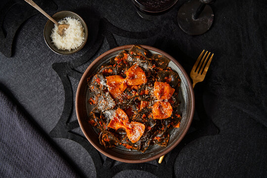 Black and orange pasta with parmesan on black table halloween season