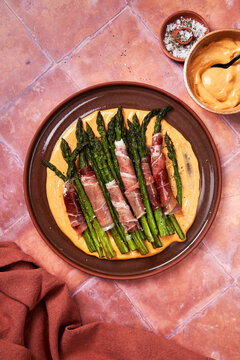 Asparagus with parma ham and aioli on plate with salt on toled background]