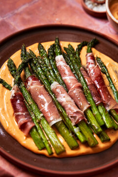 Asparagus with parma ham and aioli on plate with salt on toled background]