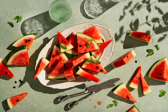 flat lay of sliced watermelon in a oval plate styled with fresh mint leaves and two glasses of sparkling water in high key