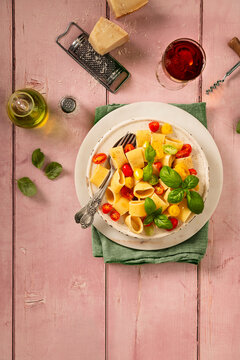 flat lay of pasta with fresh raw pachino tomatoes and basil on a pink table top with olive oil parmesan cheese and a glass of red wine