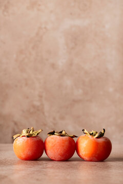 three fresh organic persimmon, in a row on a delicate background, vertical composition