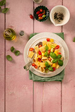 flat lay of pasta with fresh raw pachino tomatoes and basil on a pink table top with olive oil and black pepper in a mortar