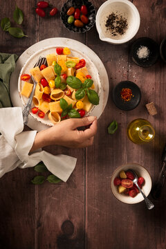 flat lay dish of macaroni with fresh raw tomatos and basil, sprinkled with black pepper, olive oil  and chilly. someone is holding the plate with her hand