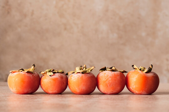 five fresh organic persimmon, in a row on a delicate background, horizontal composition
