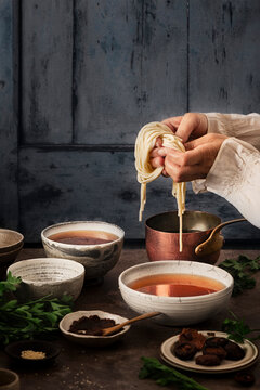 woman preparing miso soup, with noodles just boiled and shiitake mushroom in different bowls with sesam seeds and parsley