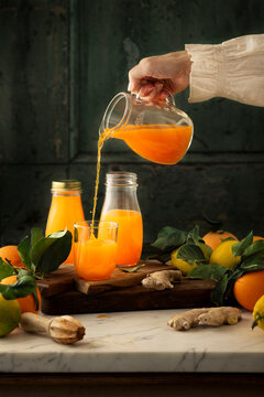 lemon and orange juice glass jars and glasses being filled by a woman  and placed on a marble table top against a green background